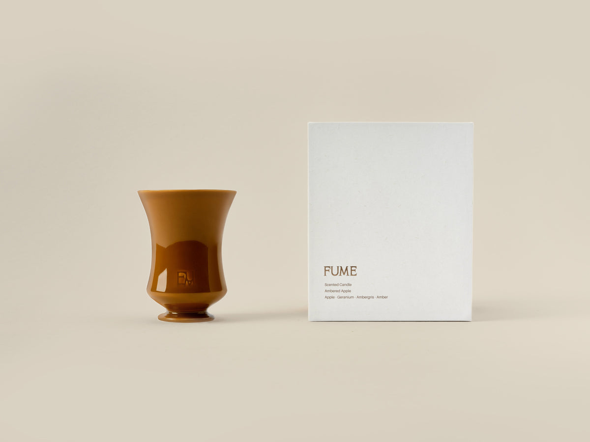 Ambered Apple candle beside its closed Fume gift box on a beige background