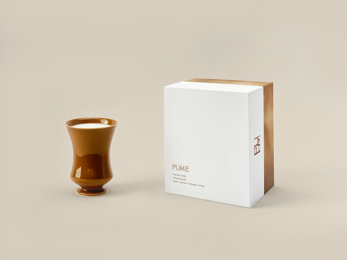 Ambered Apple candle with visible wax and wick next to its Fume gift box on a beige background