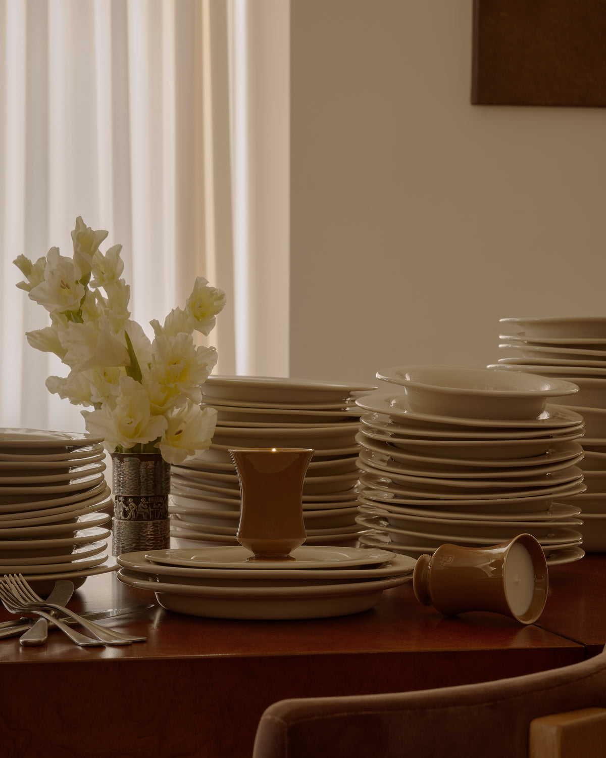 Lit Ambered Apple candle on a dining table styled with plates, a silver bowl, and white flowers