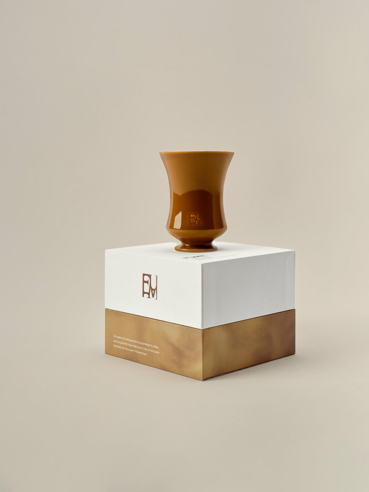 Ambered Apple candle balanced on top of its closed Fume gift box on a beige background