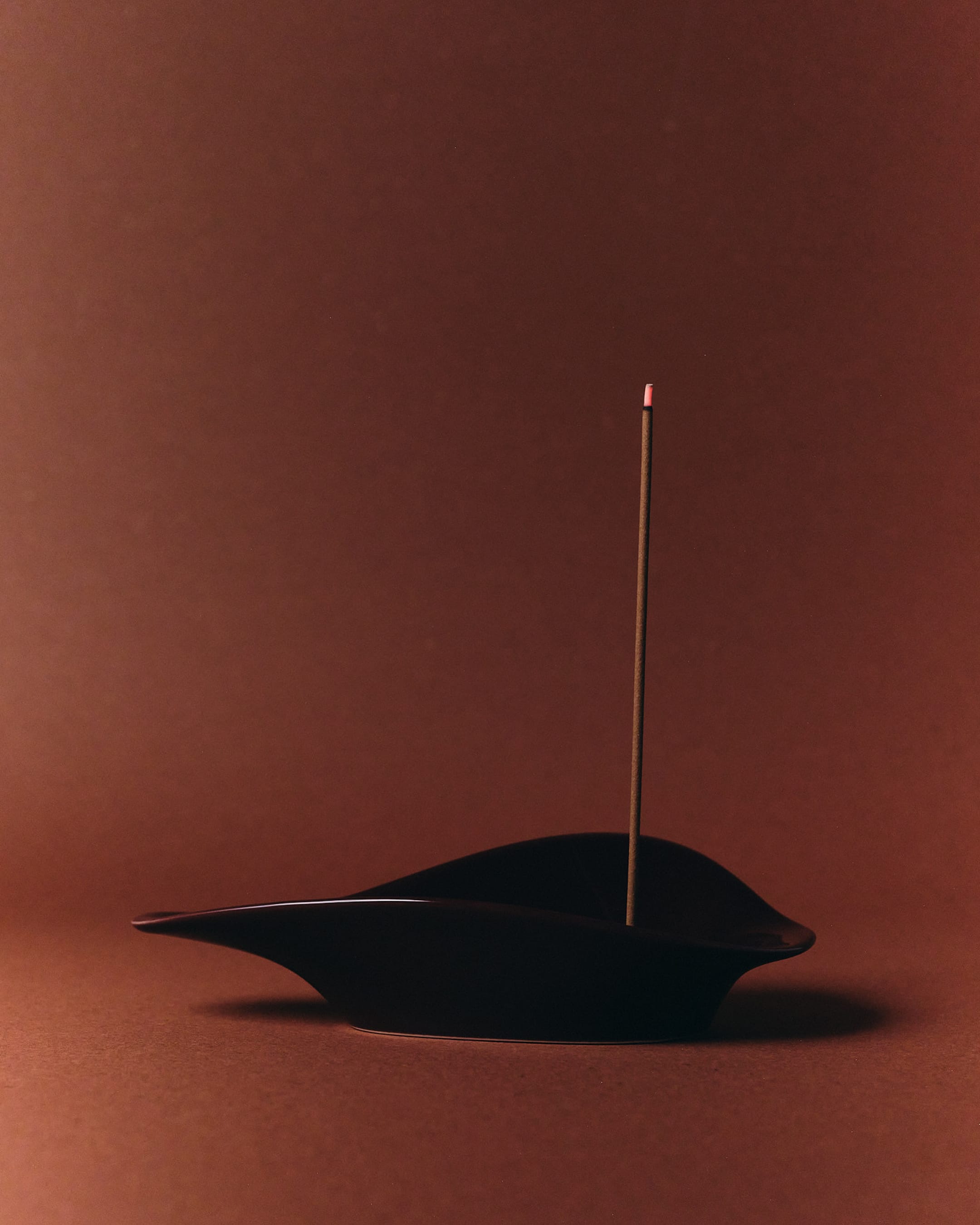 Black incense holder with a single incense stick on a brown background