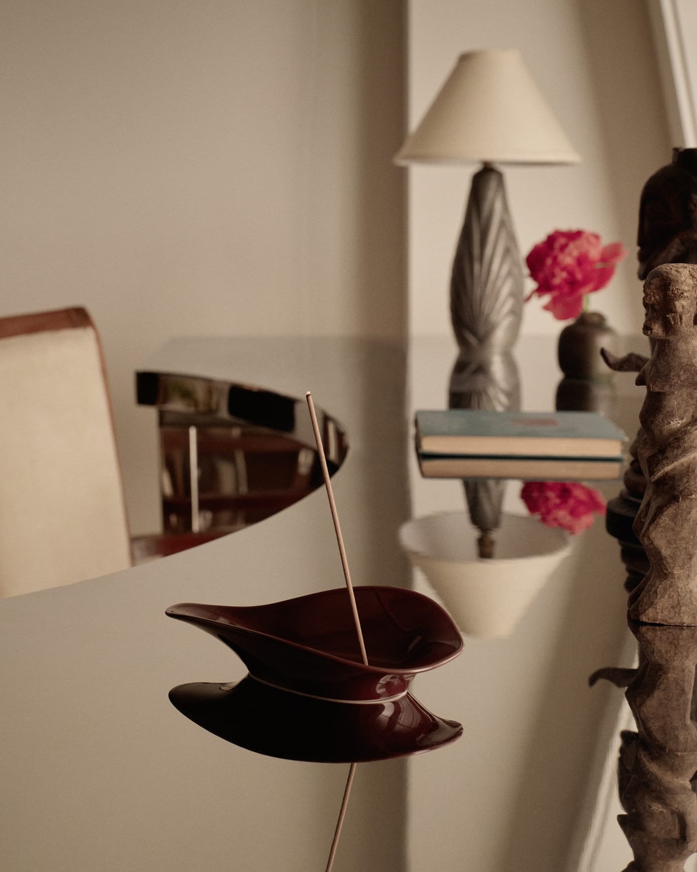 Incense burner with a single incense stick on a reflective surface, with a blurred background of a lamp and decorative items.